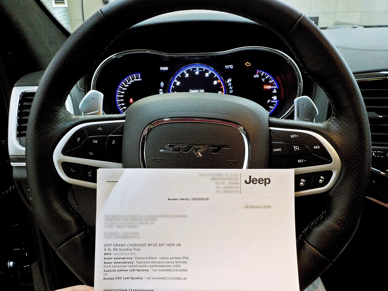 Wnętrze Jeep Grand Cherokee SRT w Sopocie z widocznym kokpitem, kierownicą i dokumentem specyfikacji pojazdu. Na desce rozdzielczej widać włączony zapłon i temperaturę 11 stopni Celsjusza.