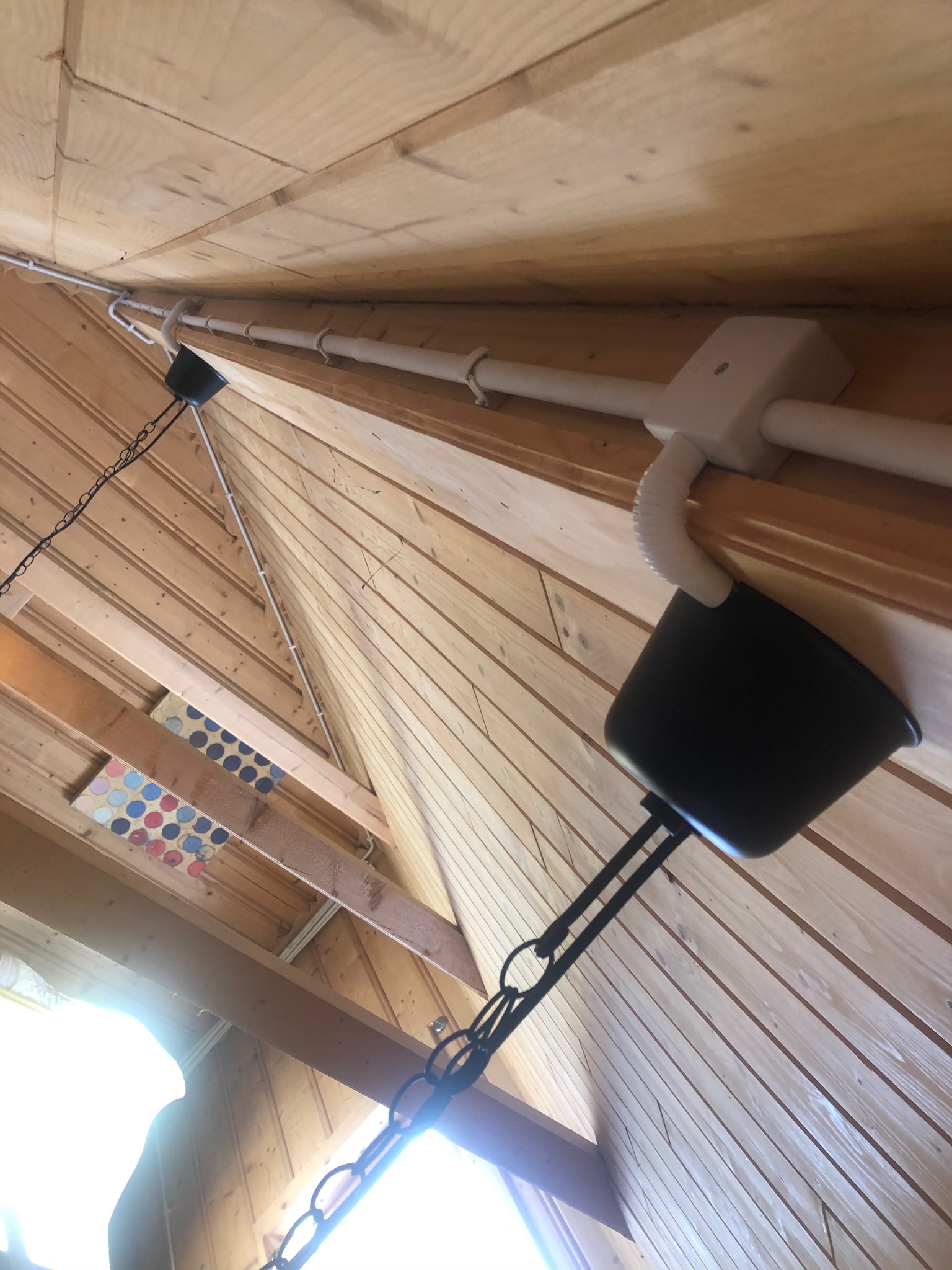 Instalacja elektryczna natynkowa w rurkach PVC, prowadzona po drewnianym stropie, z widoczną puszką instalacyjną i fragmentem zwisającej lampy z czarnym kloszem.