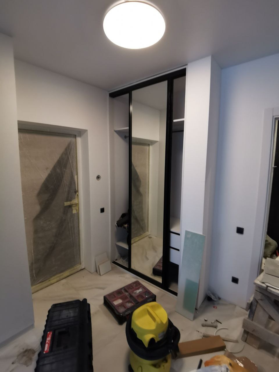 Montaż szafy przesuwnej z czarnymi ramami i lustrzanymi drzwiami w trakcie realizacji, widoczne narzędzia i elementy wykończeniowe na podłodze.