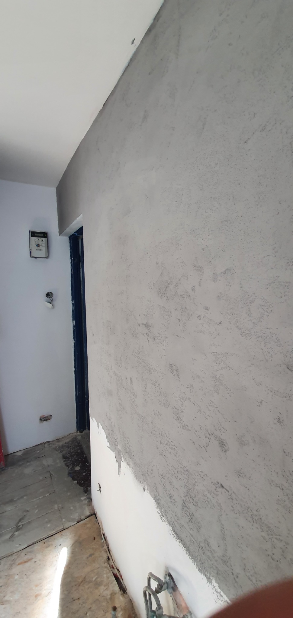 Ściana z nałożoną szarą strukturą gładzi w trakcie prac wykończeniowych w mieszkaniu w Warszawie, widoczna niedomalowana dolna część ściany i niezabezpieczona podłoga.