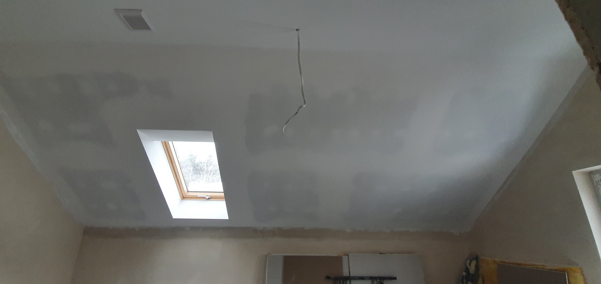 Sufit po nałożeniu gładzi, widoczne nierówności przed szlifowaniem, okno dachowe i wystający kabel.