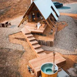 Nowoczesny domek letniskowy w kształcie litery A z drewnianym tarasem, schodami i jacuzzi na zewnątrz, widok z góry.