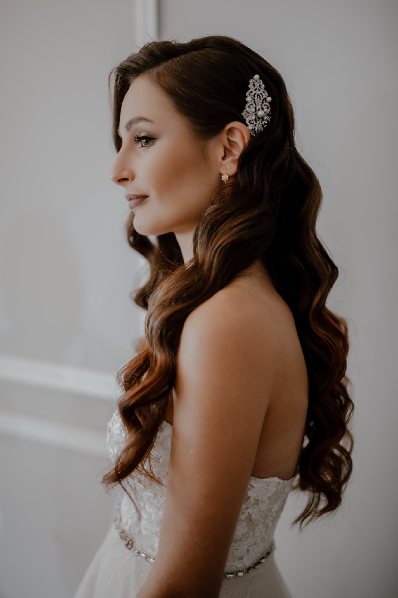 Portret kobiety z profilu, z upiętymi brązowymi włosami ozdobionymi bogatą spinką z pereł i kryształów, w sukni ślubnej z koronkowym gorsetem.