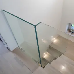 Szklana barierka zabezpieczająca schody z drewnianymi stopniami, widok z góry, minimalistyczny design.