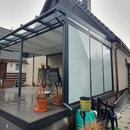 Avaso Sp. z O.O - Zadaszona konstrukcja z metalu i szkła, przylegająca do domu, z widocznymi szybami i metalowym szkieletem; dwaj mężczyźni w tle, jeden w kurtce, drugi w swetrze.