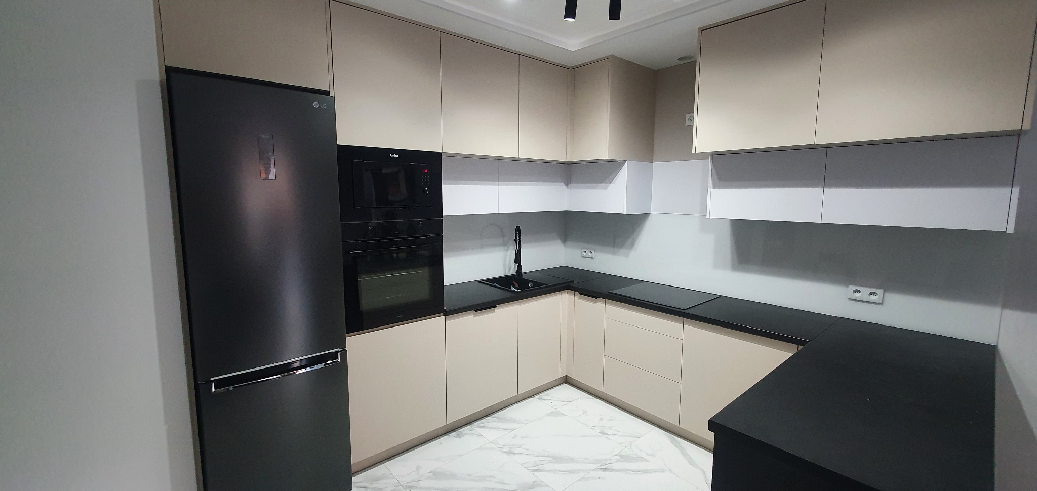 Nowoczesna kuchnia z beżowymi szafkami, czarnym blatem i sprzętem AGD, marmurowa podłoga.