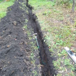 Wykopany wąski rów w ziemi na zewnątrz, z łopatą w środku i kablem na dnie.