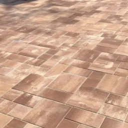 Ułożona kostka brukowa w odcieniach brązu i beżu, z widocznym krzesłem rattanowym i małą fontanną w tle.