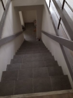 Wykończone schody wewnętrzne z szarymi płytkami, pomalowane na biało ściany i szare poręcze, widok z góry.