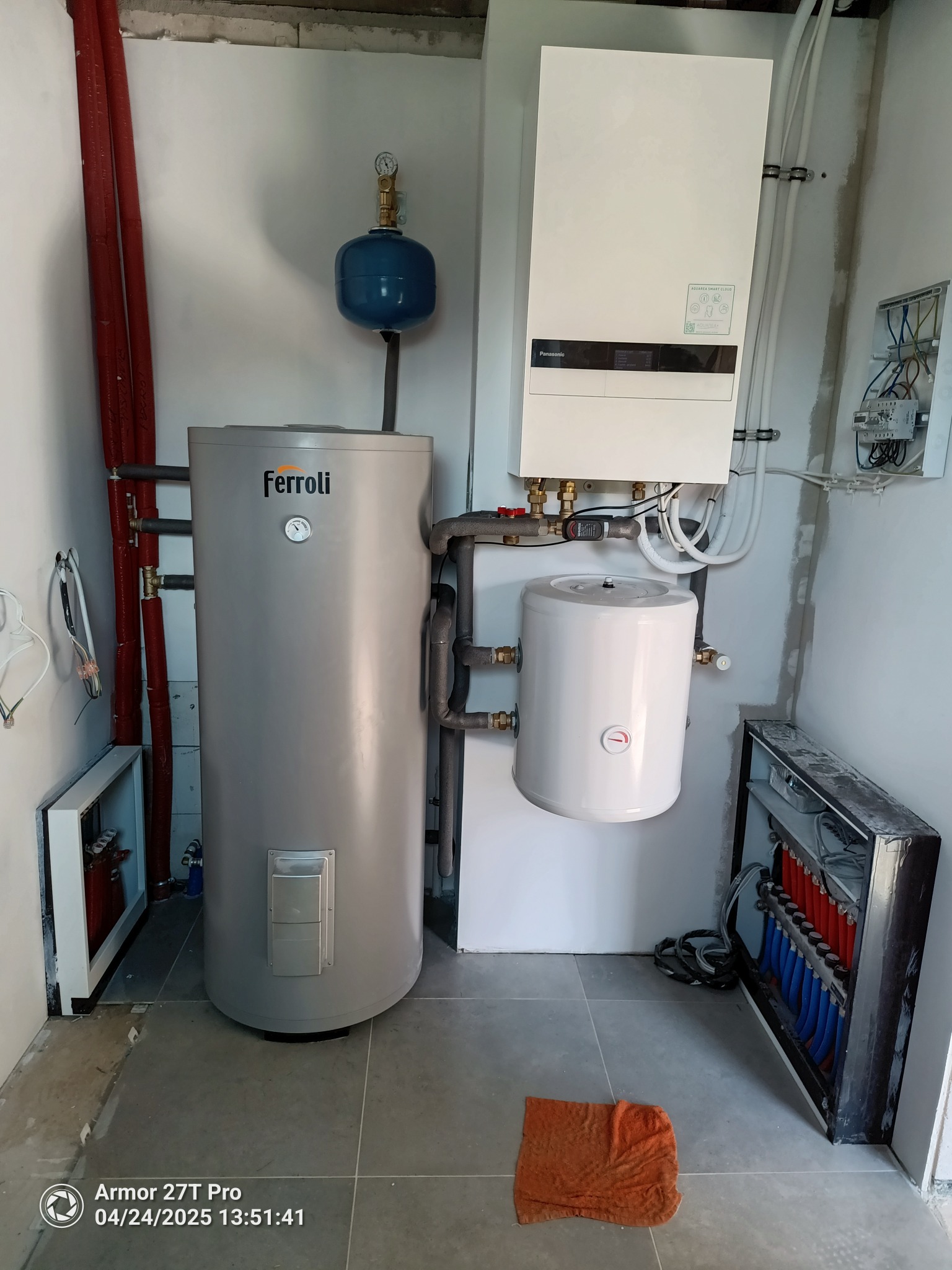 Instalacja grzewcza w kotłowni: szary zbiornik Ferroli, biały zasobnik, pompa ciepła Panasonic, rozdzielacz ogrzewania podłogowego. Pomieszczenie w stanie surowym.