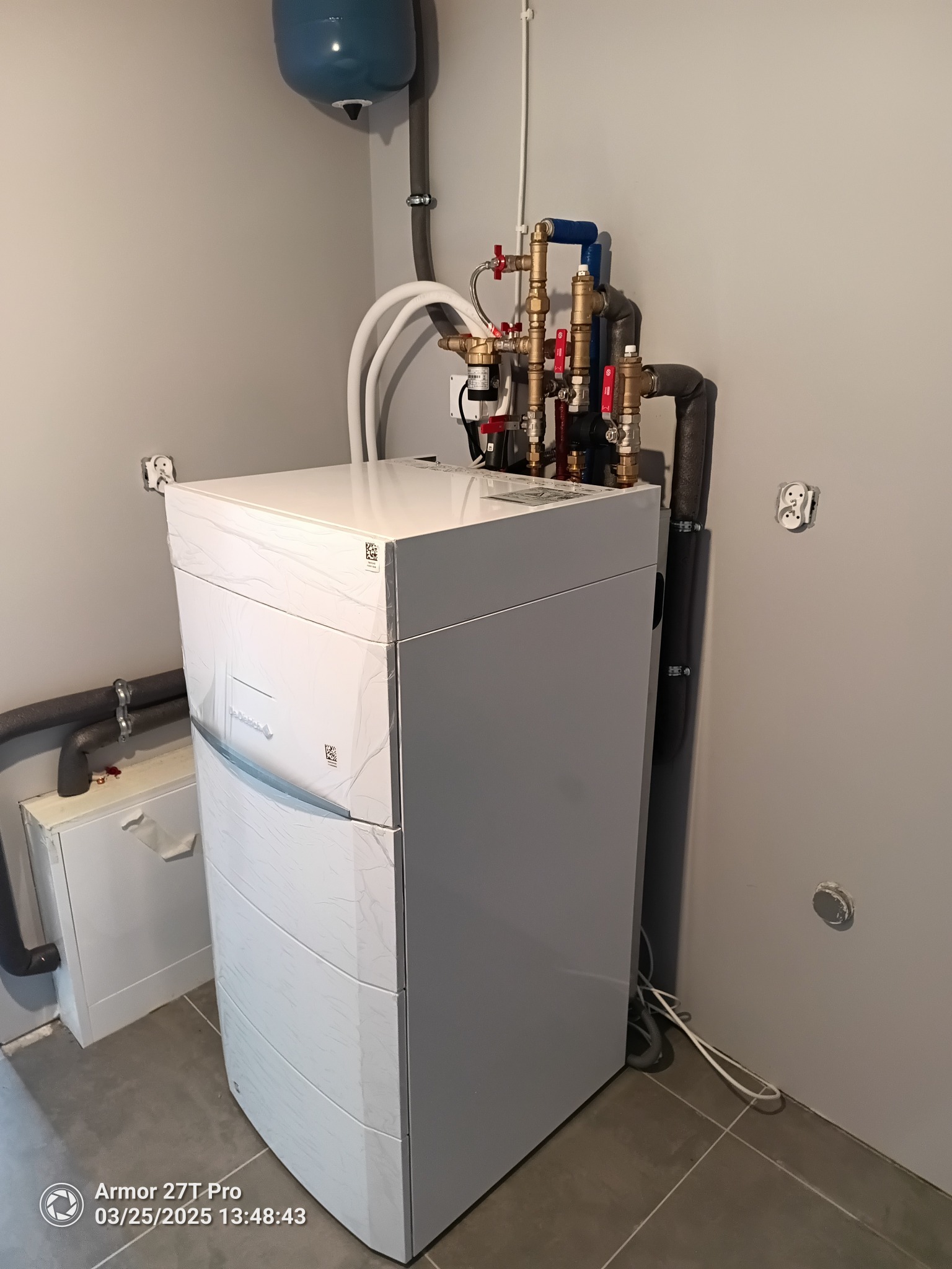 Nowoczesny, biały piec grzewczy z instalacją w pomieszczeniu technicznym w Mielcu. Widoczne rury i zawory. Minimalistyczny design, schludne wykończenie.