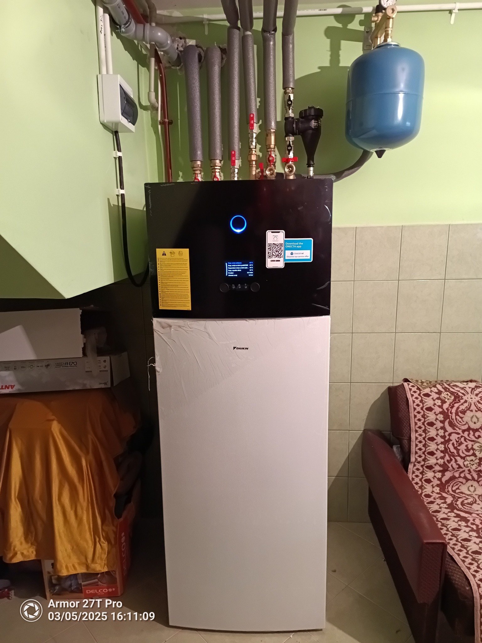 Nowoczesna pompa ciepła Daikin, z widocznymi rurami instalacyjnymi i elementami sterującymi. Domowa instalacja grzewcza w odcieniach bieli, czerni i szarości.