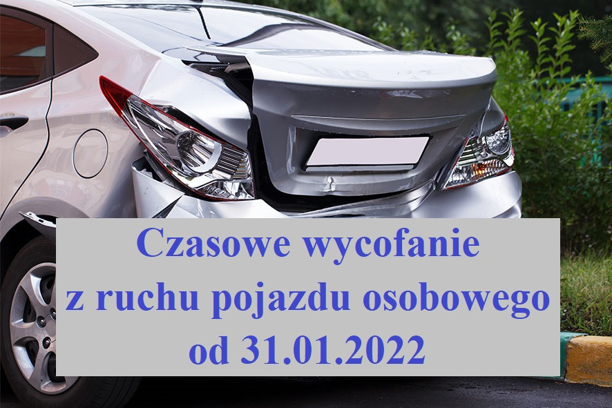 Srebrny samochód osobowy z poważnymi uszkodzeniami tylnej części nadwozia, widoczne zgniecione elementy i uszkodzony reflektor. Tło stanowi zieleń krzewów i fragment chodnika.