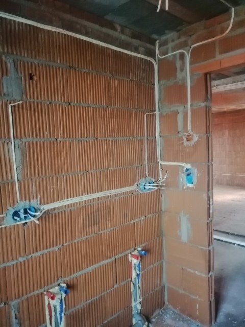 Wewnętrzna instalacja elektryczna w trakcie montażu w surowym budynku z cegły, widoczne przewody w peszlach i puszki instalacyjne w ścianach.