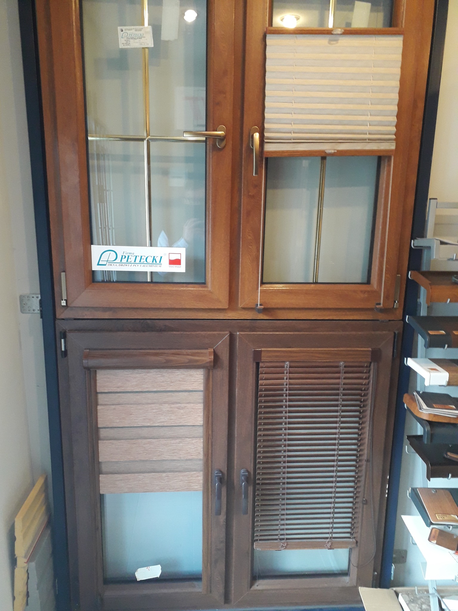 Wystawa okien PCV i aluminiowych z zamontowanymi różnymi typami żaluzji: aluminiowymi i dzień noc, z naklejoną naklejką producenta.