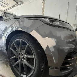 Szary Range Rover Velar w trakcie naprawy blacharskiej: przedni błotnik i zderzak z nałożoną szpachlą, przygotowane do lakierowania.
