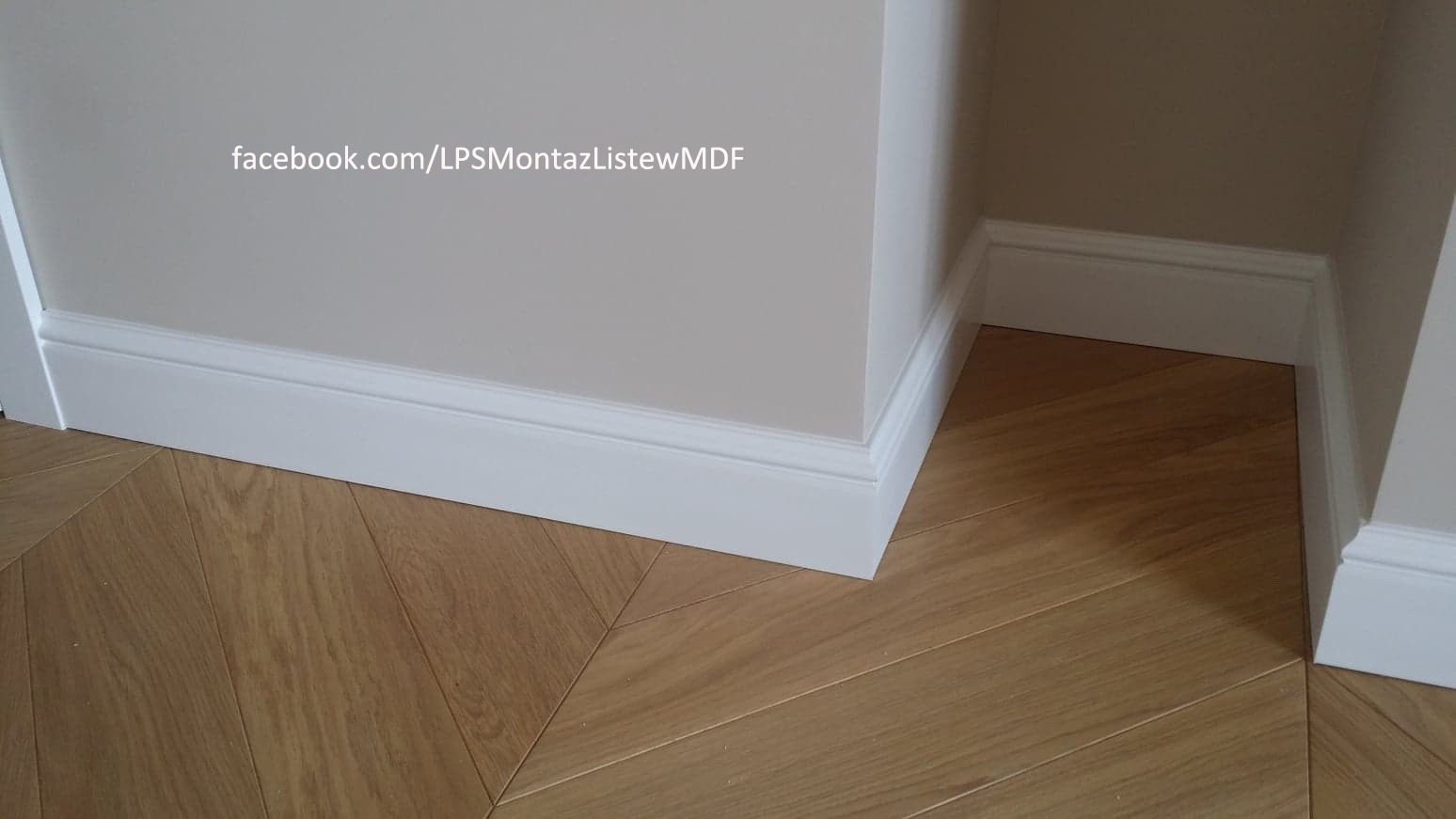 Zamontowane białe listwy przypodłogowe MDF przy ścianie i parkiecie ułożonym w jodełkę, widoczny narożnik. Na ścianie widoczny adres strony internetowej.