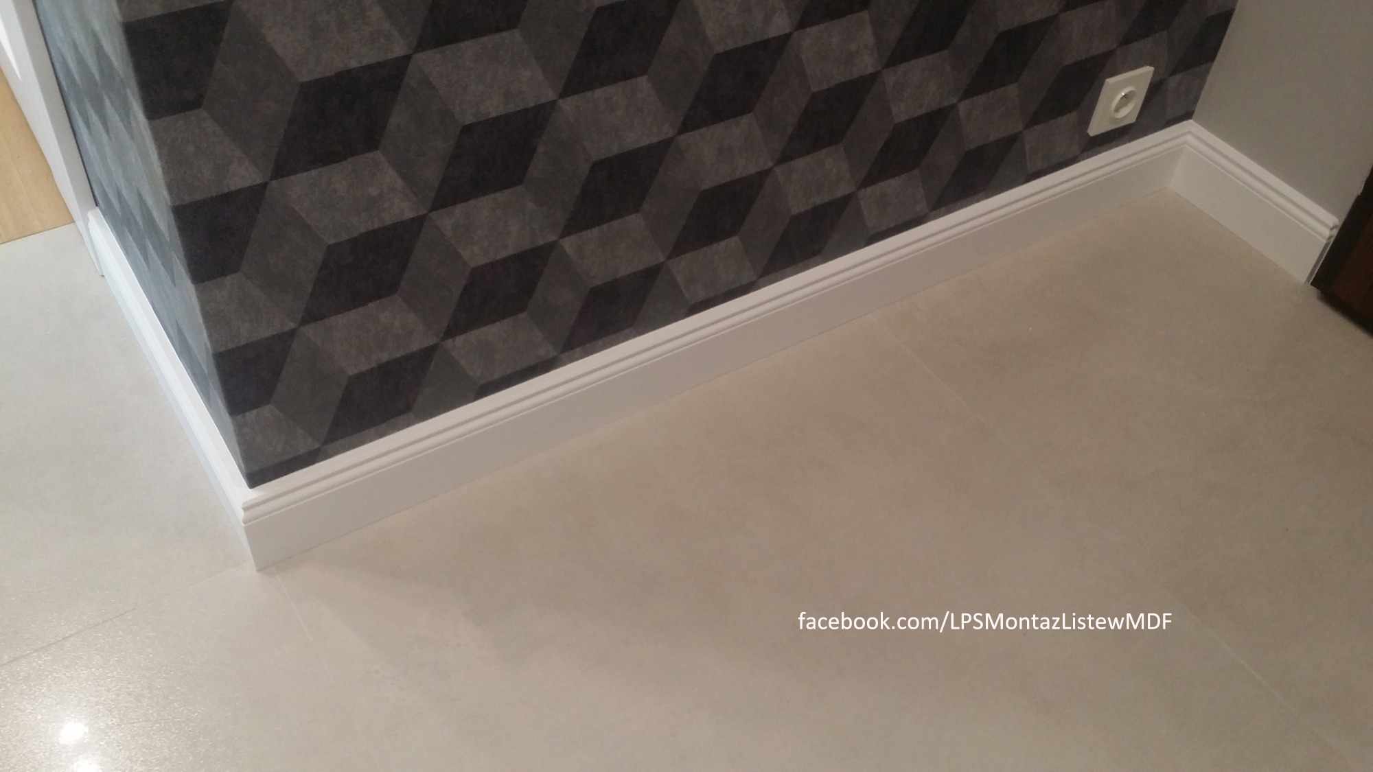 Zamontowane białe listwy przypodłogowe MDF na styku ściany z geometryczną tapetą i jasnej podłogi z płytek. Widoczny fragment gniazdka elektrycznego.