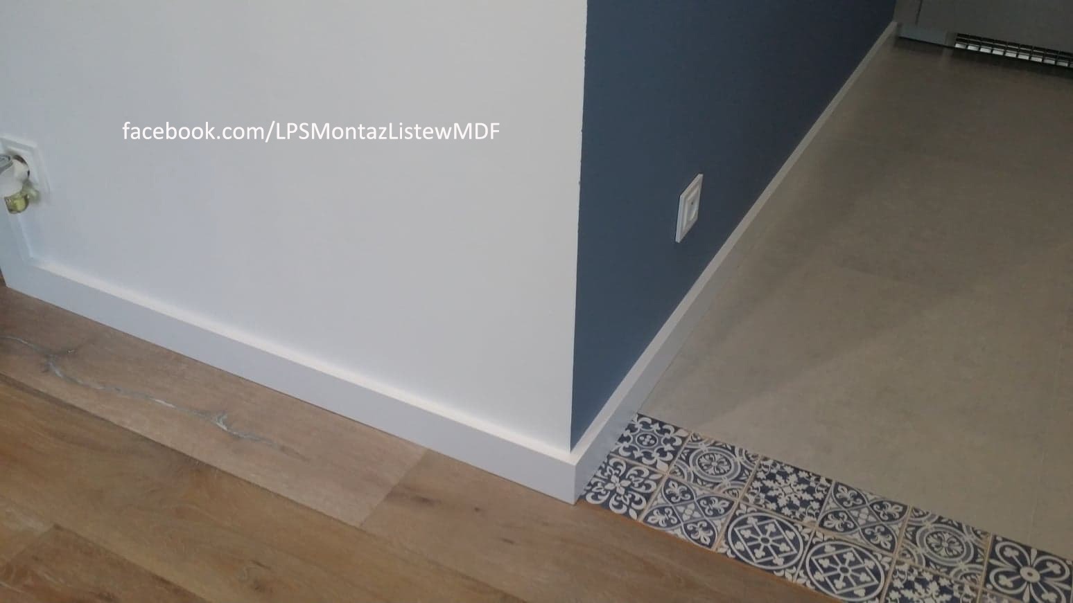 Połączenie paneli podłogowych z płytkami dekoracyjnymi przy ścianie pomalowanej na biało i granatowo, wykończone białą listwą przypodłogową.