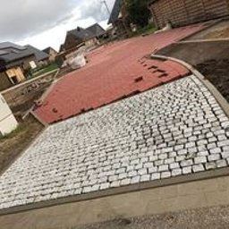 ExpertBruk Brukarstwo Roboty Ziemne - Fragment nowo ułożonej nawierzchni z kostki brukowej w dwóch kolorach: szarej i czerwonej. Szara kostka ułożona w regularny wzór, czerwona w nieregularny. Widoczny obrzeże i przygotowane podłoże.