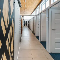 Wnętrze sklepu z drzwiami, prezentacja r&oacute;żnych modeli drzwi wewnętrznych i zewnętrznych, widoczne drzwi przesuwne z dekoracyjnym wzorem, rząd białych drzwi z ościeżnicami, drewniany sufit...