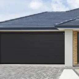 Nowoczesna, grafitowa brama garażowa segmentowa z poziomymi przetłoczeniami, zamontowana w budynku z ceglaną elewacją i szarą dachówką.