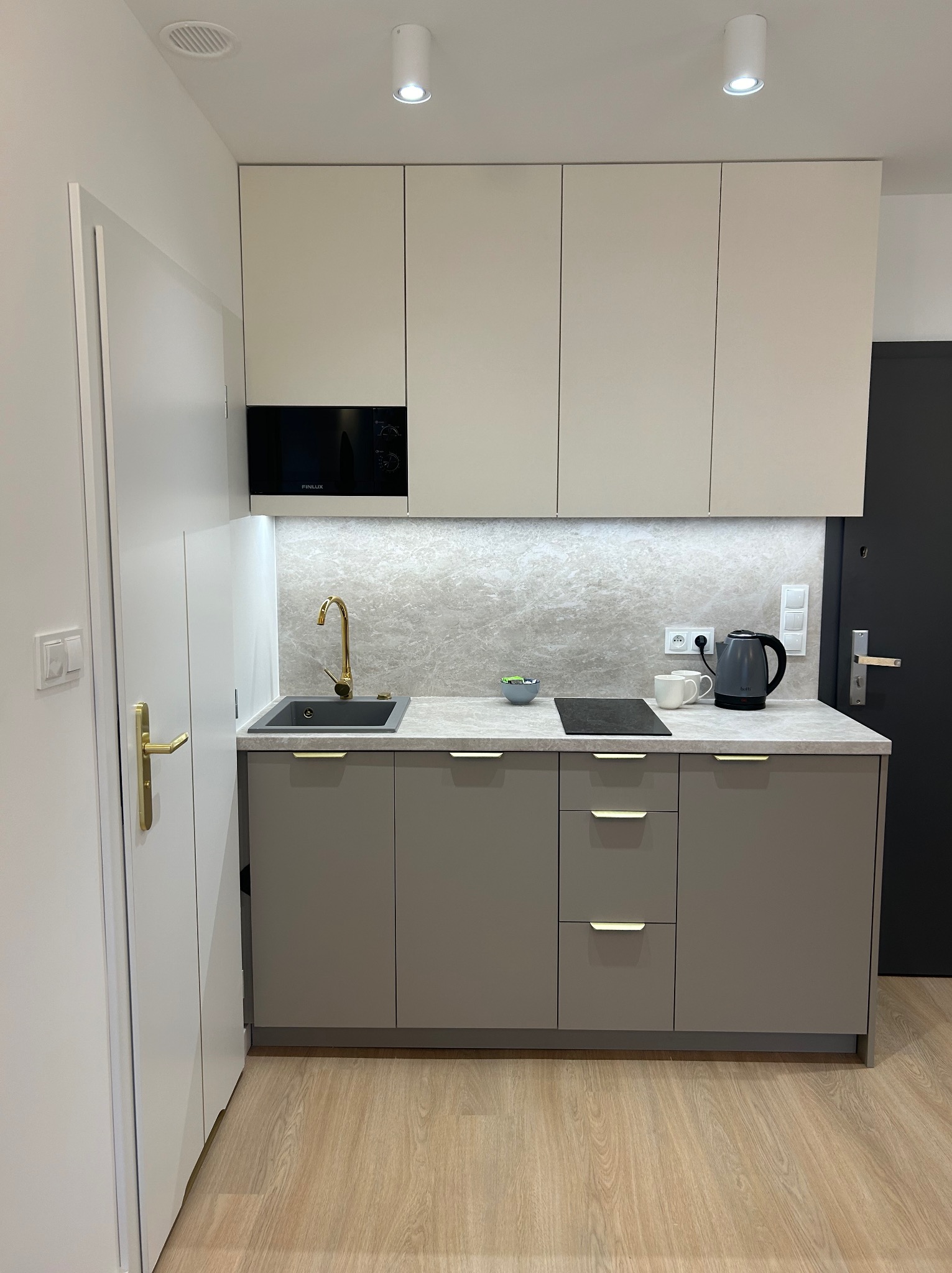 Nowoczesna, jasna kuchnia w odcieniach beżu i szarości z złotą armaturą, minimalistycznym designem i płytą indukcyjną.