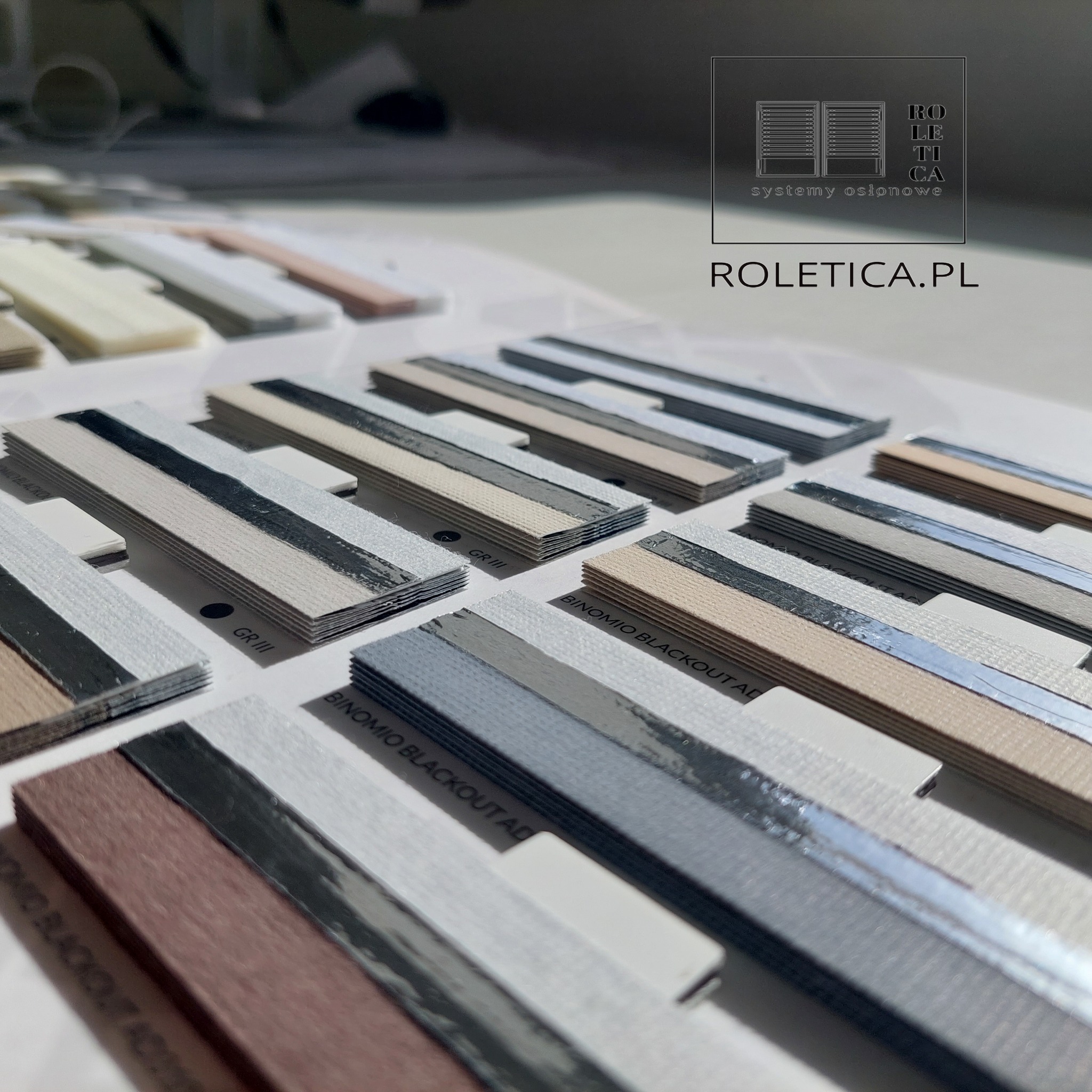 Paleta próbek materiałów do systemów osłonowych okien, z widocznym logo firmy Roletica.pl w prawym górnym rogu.