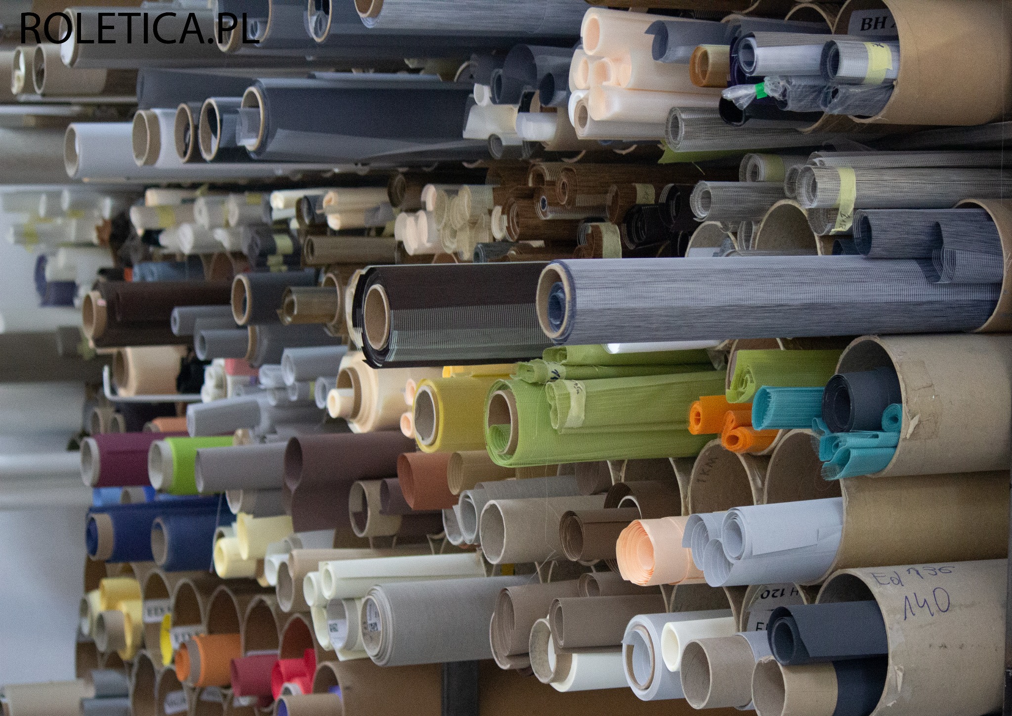 Magazyn tkanin Roletica.pl: półki wypełnione rolami materiałów w różnych kolorach i fakturach, przeznaczonych do produkcji rolet na wymiar.