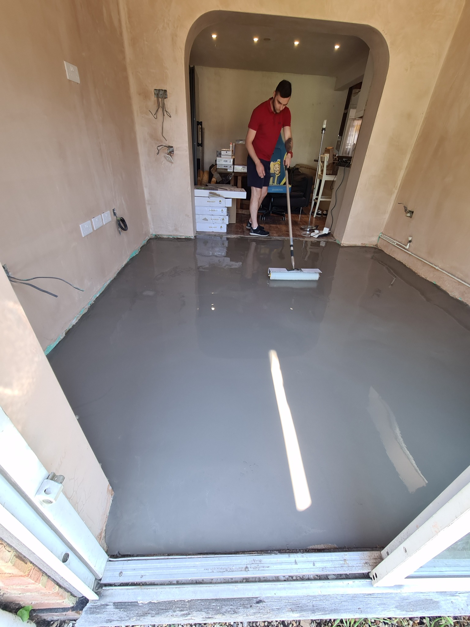 Wylewka samopoziomująca rozprowadzana wałkiem w pomieszczeniu z przygotowanymi ścianami, widoczne puszki elektryczne i listwy przy podłodze.