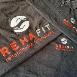 Czarna koszulka i polo z wyhaftowanym logo i napisem 'REHAFIT rehabilitacja funkcjonalna', widoczne detale haftu i faktura materiału.