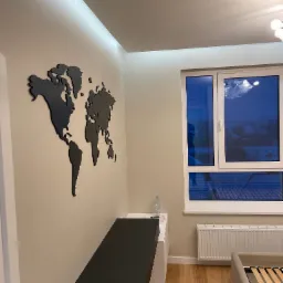 Nowoczesny pokój z drewnianą podłogą, czarną mapą świata na ścianie, oświetleniem LED w suficie i widokiem na zewnątrz przez okno.