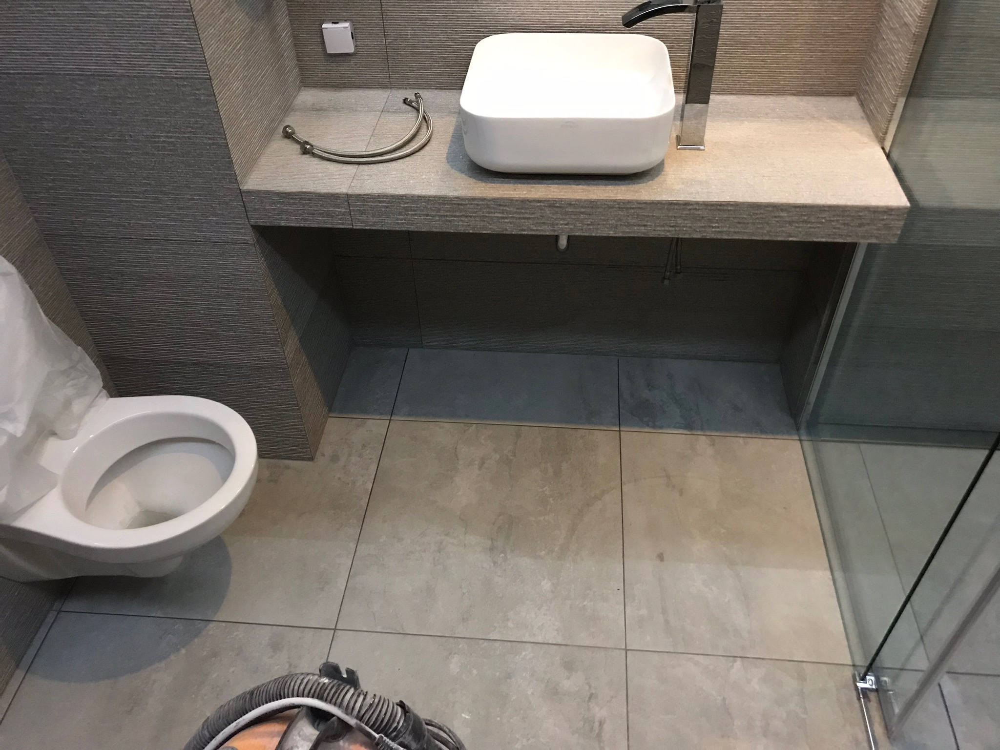 Nowoczesna, szara łazienka z umywalką nablatową i toaletą w Przasnyszu, widok z góry na podłogę z szarych płytek i fragment kabiny prysznicowej.