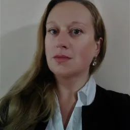 Portret kobiety w białej koszuli i czarnej marynarce, z kolczykiem z przezroczystym kamieniem.