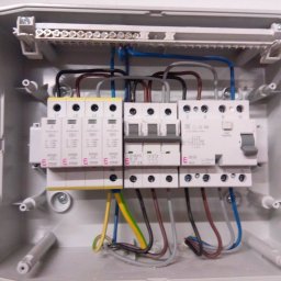 Sol Fin - Otwarta skrzynka elektryczna z zainstalowanymi bezpiecznikami, ogranicznikami przepięć i okablowaniem w kolorach niebieskim, brązowym, szarym i żółto-zielonym.