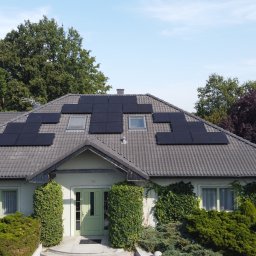 Sol Fin - Dom jednorodzinny z szarym dachem, na którym zamontowano panele słoneczne w kilku sekcjach, z pracownikiem na dachu w tle.