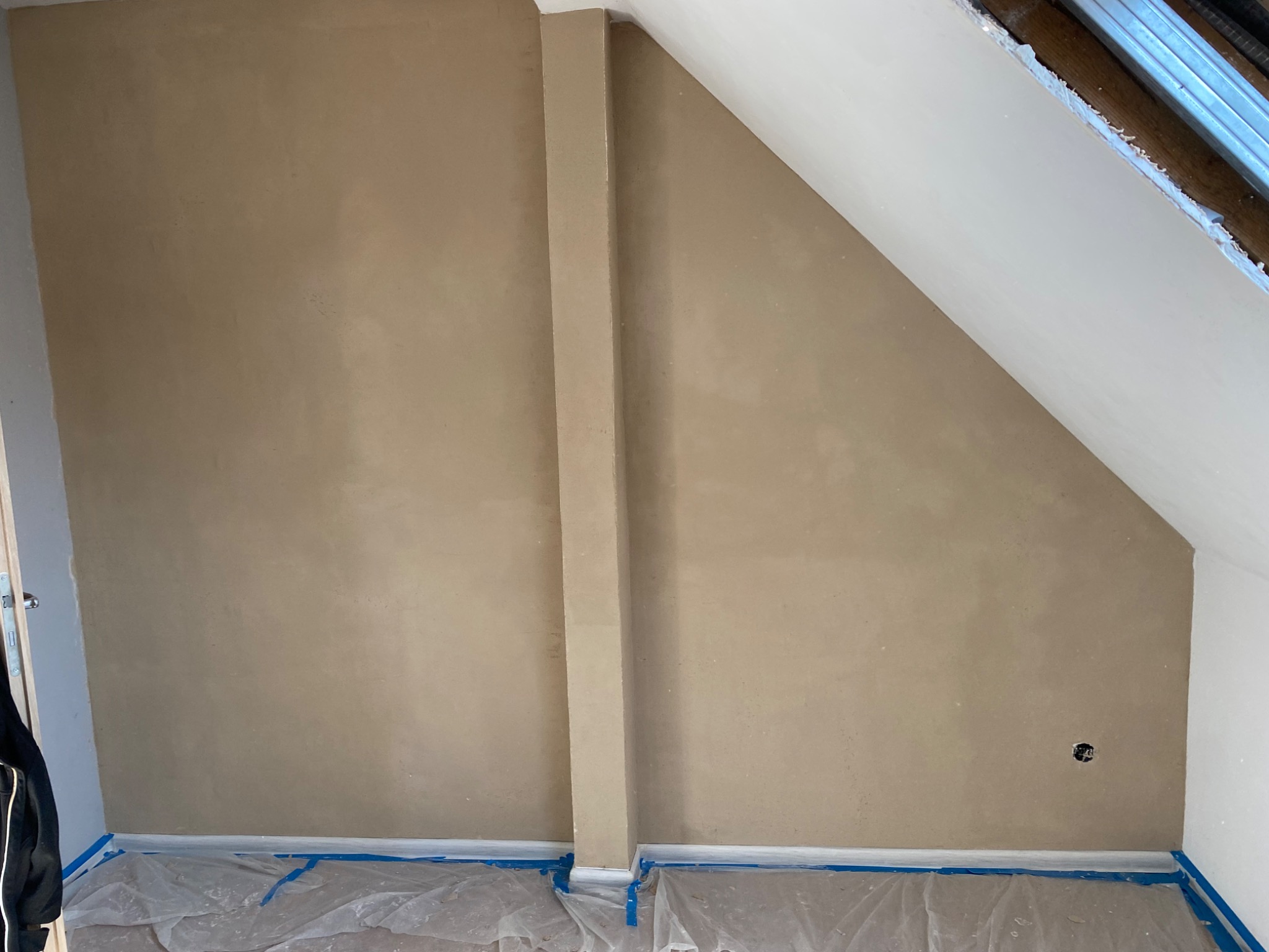Poddasze po nałożeniu szpachli, ściany w kolorze beżowym, zabezpieczona folia malarska na podłodze, widoczna puszka elektryczna
