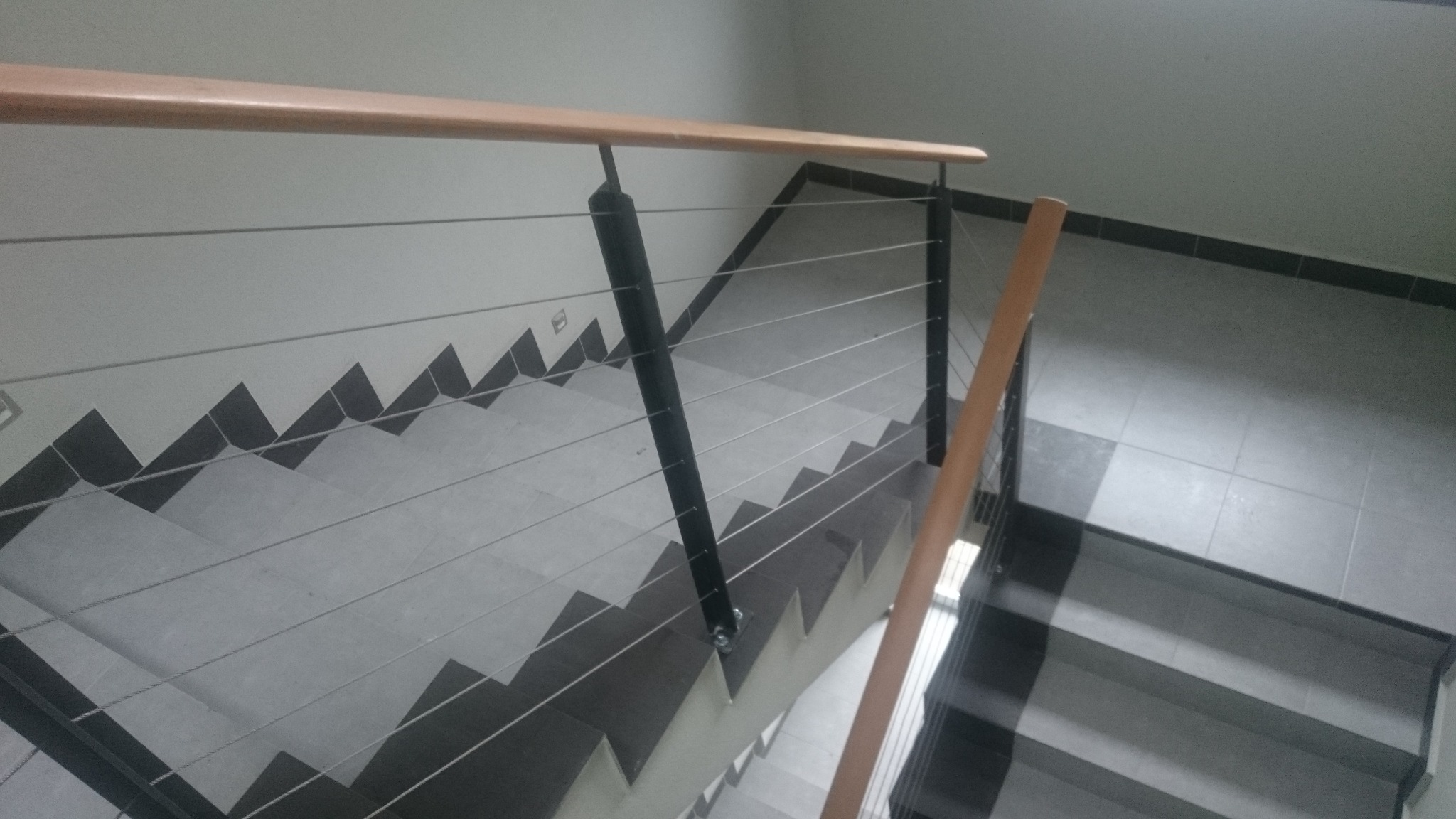 Schody wykończone płytkami z balustradą z poziomych linek stalowych, drewnianym poręczą i czarnymi słupkami, widok z góry.