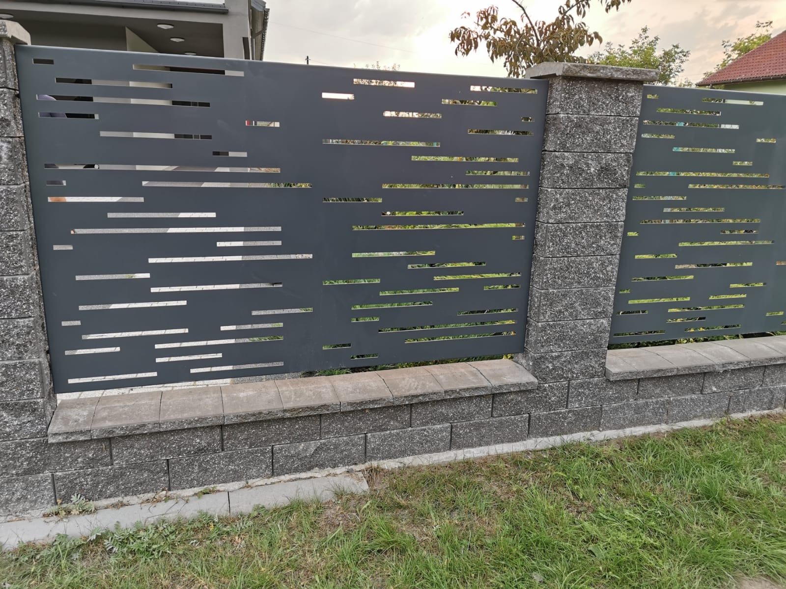 Nowoczesne ogrodzenie z szarego metalu z poziomymi wycięciami, wsparte na słupkach z szarej kostki, Bielsko-Biała.