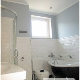 Płytkarz Wrocławski - Retro łazienka z czarną wanną na nóżkach, białe płytki typu metro na ścianach, kabina prysznicowa z przezroczystego szkła, logo firmy na pierwszym planie.