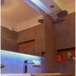 Płytkarz Wrocławski - Nowoczesna łazienka z szarymi płytkami, podwójnym prysznicem deszczownicą i podświetleniem LED, widoczny fragment blatu z logo firmy.