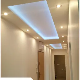 Korytarz z podwieszanym sufitem z podświetleniem LED, punktowe oświetlenie halogenowe, widok w kierunku drzwi do łazienki w trakcie remontu.