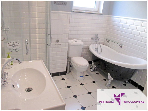 Retro łazienka z białą armaturą, czarną wanną na ozdobnych nogach i białymi płytkami typu metro na ścianach oraz czarno-białą podłogą w romby.