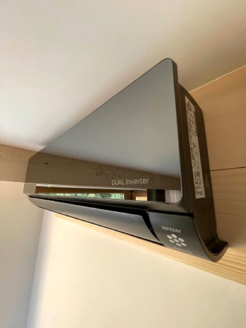 Czarny klimatyzator typu split z napisem 'Dual Inverter' i logo 'Ionizer' zamontowany na drewnianej belce pod sufitem.