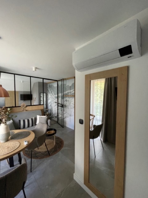 Nowoczesny klimatyzator ścienny w jasnym salonie z lustrem i szklaną ścianą działową