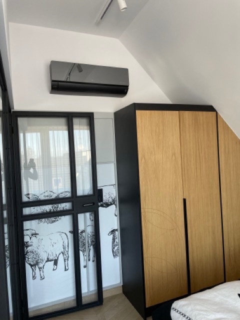 Nowoczesny, czarny klimatyzator ścienny w sypialni ze ścianą w owce i drewnianą szafą.