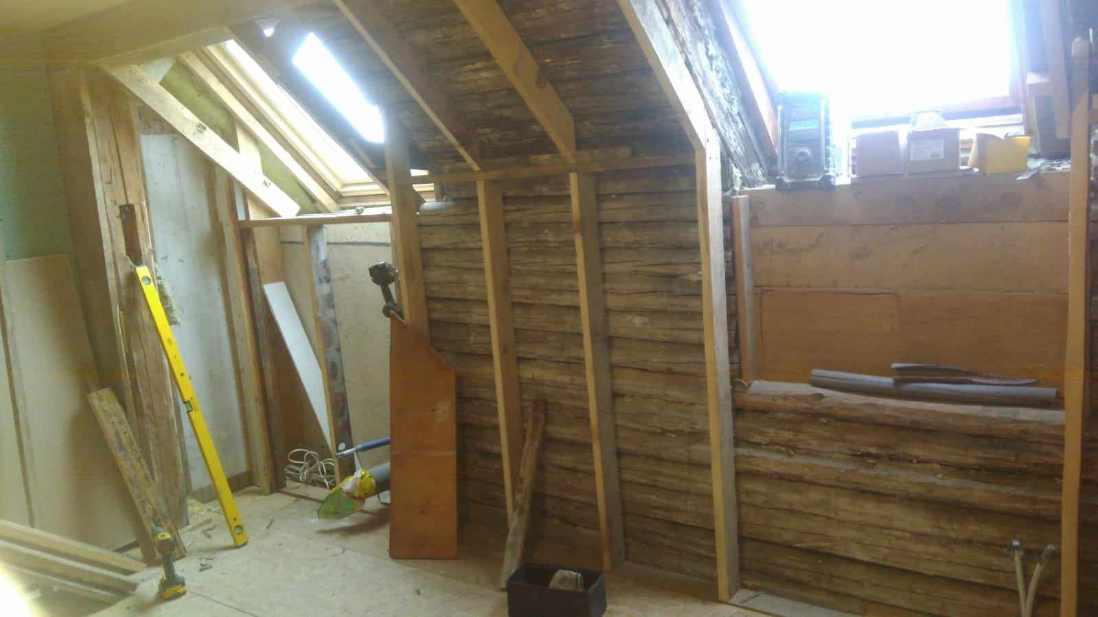 Remont poddasza: widok na drewnianą konstrukcję ścian i sufitu, z oknem dachowym i narzędziami pracy, w trakcie prac wykończeniowych.