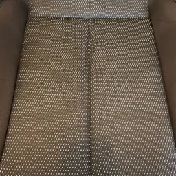 Wnętrze samochodu: czarno-szare siedzenie z drobnym wzorem w romby, widoczne z góry, z ciemną, gładką tapicerką po bokach.