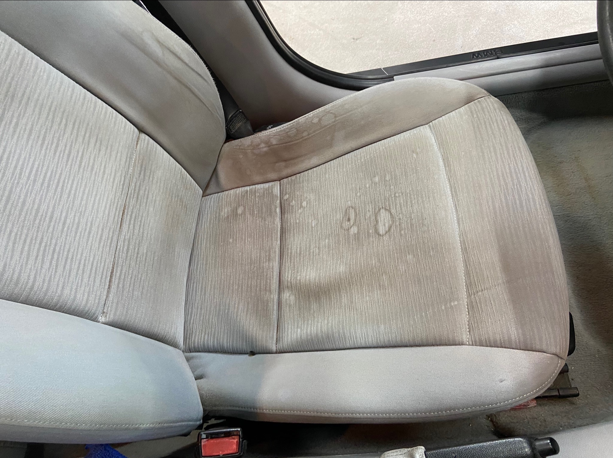 Beżowy fotel samochodowy z widocznymi plamami przed czyszczeniem tapicerki.