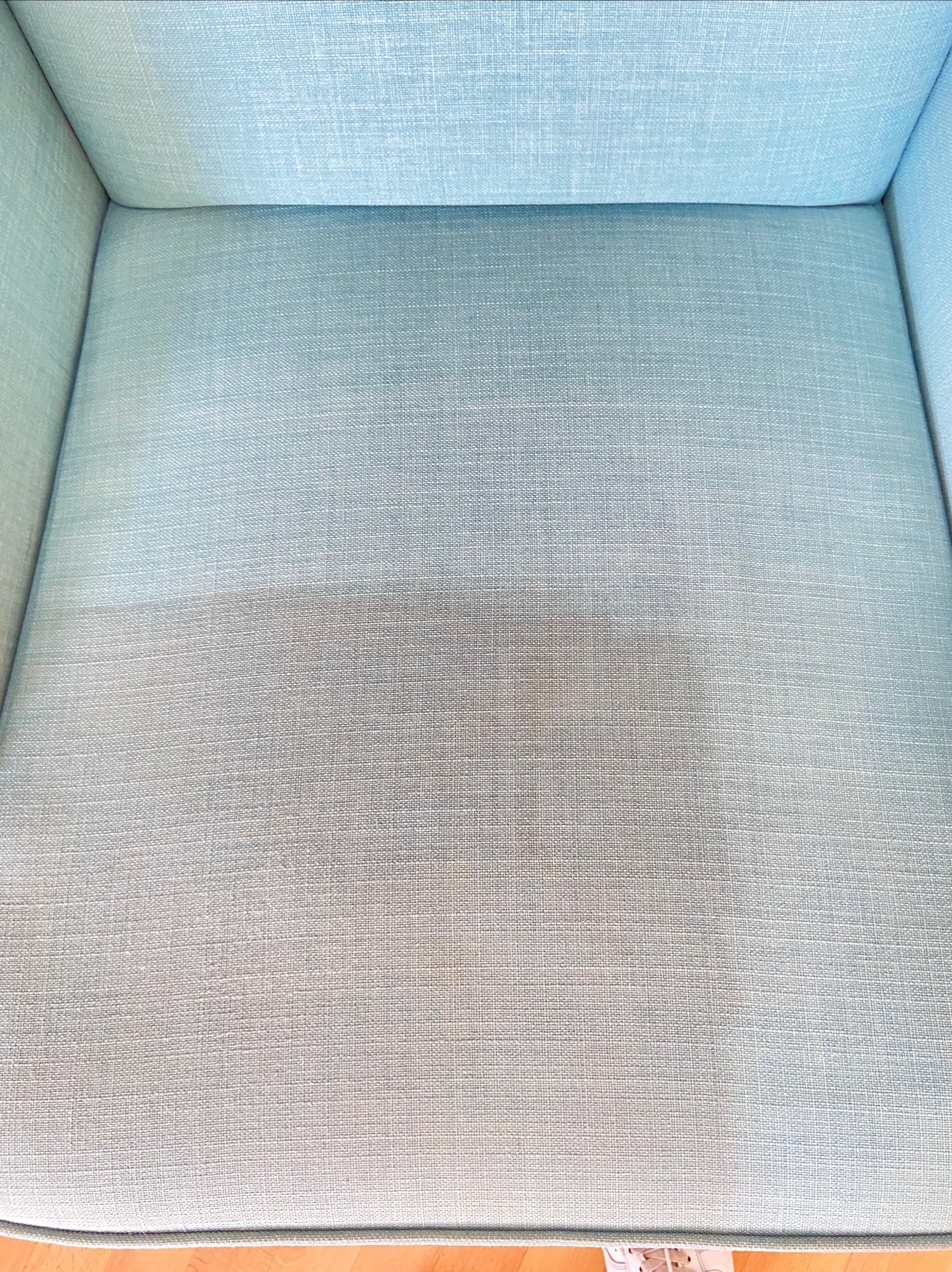 Fragment siedziska fotela obitego jasnoniebieską tkaniną, widoczna wyraźna różnica w czystości pomiędzy wypraną a niewypraną częścią, ukazująca skuteczność czyszczenia.